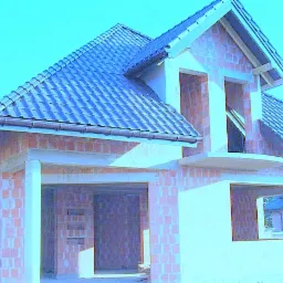 Dom w trakcie budowy z widoczną konstrukcją dachu pokrytą ciemną dachówką, ściany z czerwonej cegły i niezamontowane okna, garaż w stanie surowym otwarty.